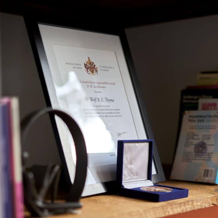 On aperçoit quelques-uns des diplômes et des prix reçus par Wolf Thyma au milieu des ouvrages de droit, de psychiatrie, de recettes de cuisine et de poésie haïtienne.